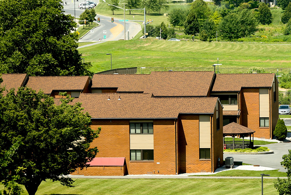 Housing is available to Penn State College of Medicine students, residents and postdocs in University Manor East and West apartment complexes. One of the complexes is pictured as seen from a higher floor of a nearby building, with a road and trees framing it in the background.