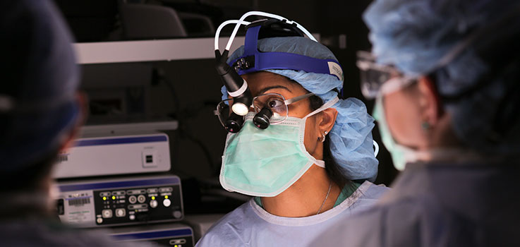 Dorothy V. Rocourt, MD, surgeon at Penn State Health Milton S. Hershey Medical Center, is seen in the operating room at the Medical Center in October 2014. She is pictured wearing a surgical mask and blue surgical scrubs, with the back of another surgeon in scrubs seen to the right of the photo.