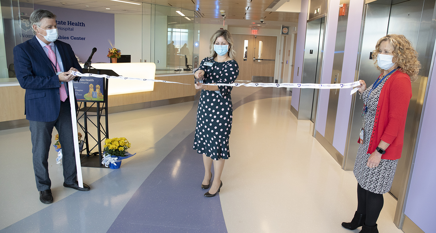 Dr. Richard Legro holds one end of a Penn State Health ribbon while Dr. Jaimey Pauli cuts the ribbon to celebrate the completion of an expansion of Penn State Health Children's Hospital.