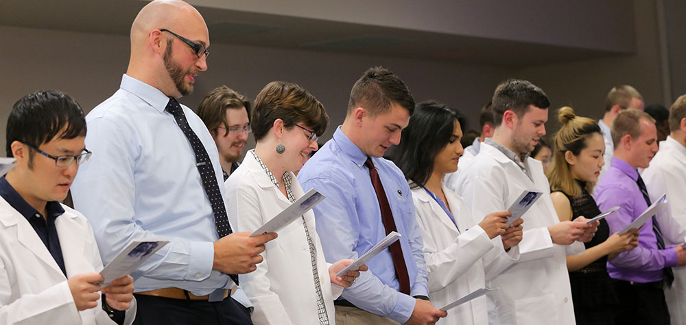 Penn State graduate students, including those from the Department of Public Health Sciences, participate in the ninth annual Graduate Student Oath Ceremony on August 18, 2017. The students are pictured standing in a line, reading from a program.