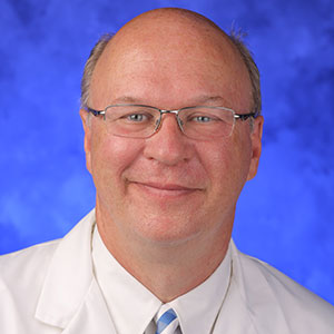 Mack Thomas Ruffin IV, MD, MPH, is Chair of the Department of Family and Community Medicine at Penn State College of Medicine. He is pictured wearing a white dress shirt and dark tie, as well as a white medical coat, in front of a blue photo background.