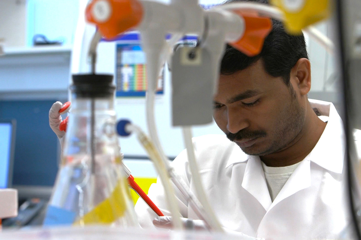 A researcher looks down while working in a lab; laboratory equipment is in the foreground.