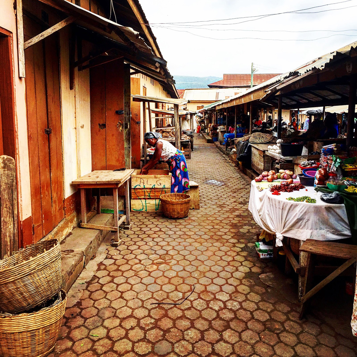 Wooden buildings and market stalls in Ghana with a woman reaching into a box.