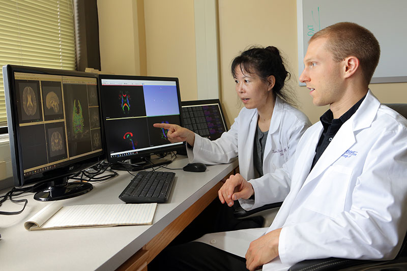 Nicholas Sterling, a student in the MD/PhD Program at Penn State College of Medicine, works with faculty member Xuemei Huang to investigate pictures of brain scans on a computer. Huang is pointing toward the screen as Sterling looks on.