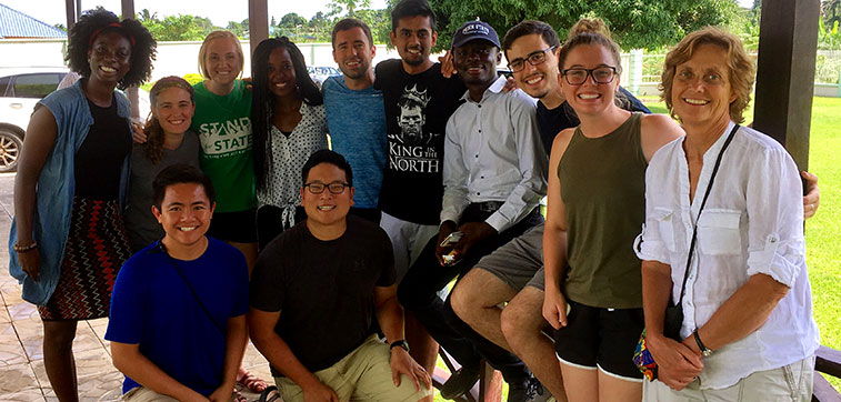 Students in the Global Health Scholars Program at Penn State College of Medicine traveled to Ghana in June 2016. Here, a group of students is pictured during a traditional welcoming ceremony conducted by a Ghanaian village chief, who is pictured at front with Ghanaian men on either side of him and the students behind them. They are outside on a porch.