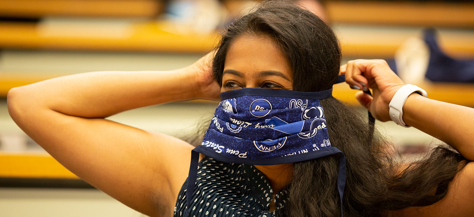 A Penn State College of Medicine medical student is seen during the 2020 orientation. She is tying a Penn State-themed mask.