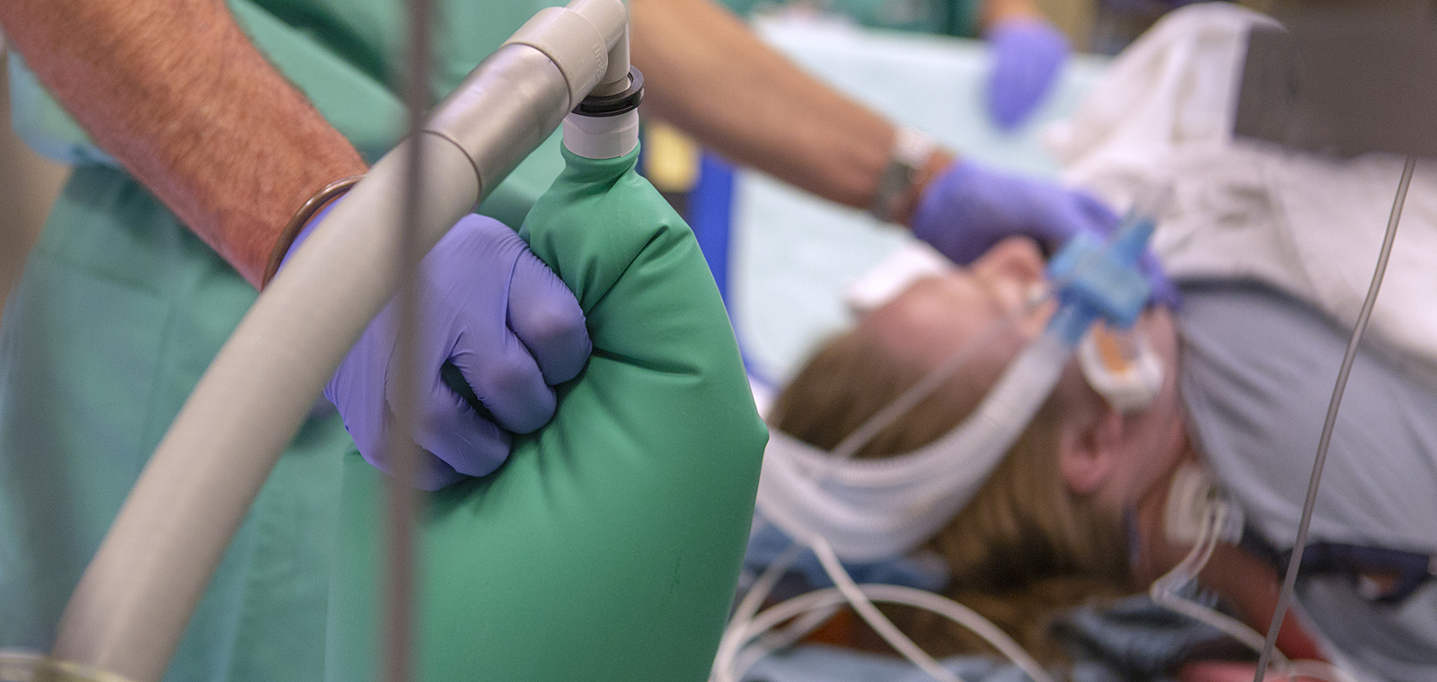 Close-up of a gloved hand holding an anesthesiology tool with a blurred patient in the background.