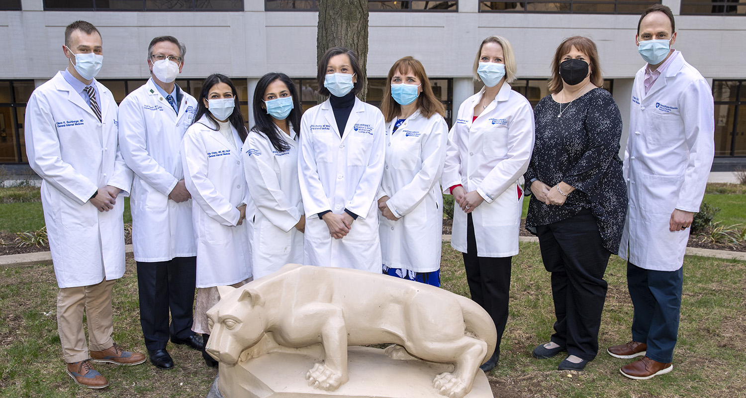 Dr. Glenn Buchberger, Dr. Paul Haidet, Dr. Alia Chisty, Dr. Eliana Hempel, Dr. Cynthia Chuang, Dr. Jennifer McCall-Hosenfeld, Dr. Jennifer Kraschnewski, lead administrative associate Tami Cassel and physician assistant Eric Patten pose for an outdoor group photo in front of a statue of a lion.