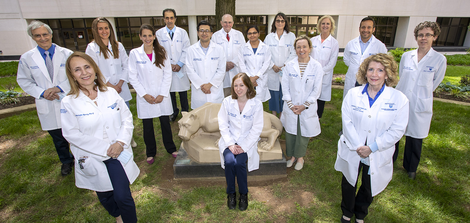 Fifteen members of the Division of Infectious Diseases and Epidemiology, all wearing white coats, gather for a group photo outside on the campus of Penn State College of Medicine.