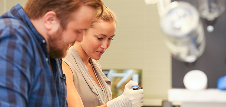 Michael Ludwig and Caitlin McMenamin, both students in the Anatomy Graduate Program at Penn State College of Medicine, are seen at work in a lab in the Department of Neural & Behavioral Sciences. The two are looking downward and framed at right by clean glassware hanging on a lab wall.