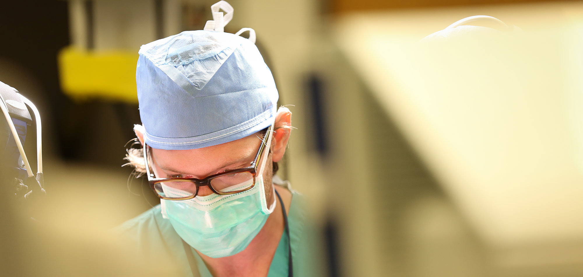 Brad Zacharia, MD, MS, assistant professor of neurosurgery, is seen in the operating room in 2015. He is wearing a mask, hair covering and scrubs.