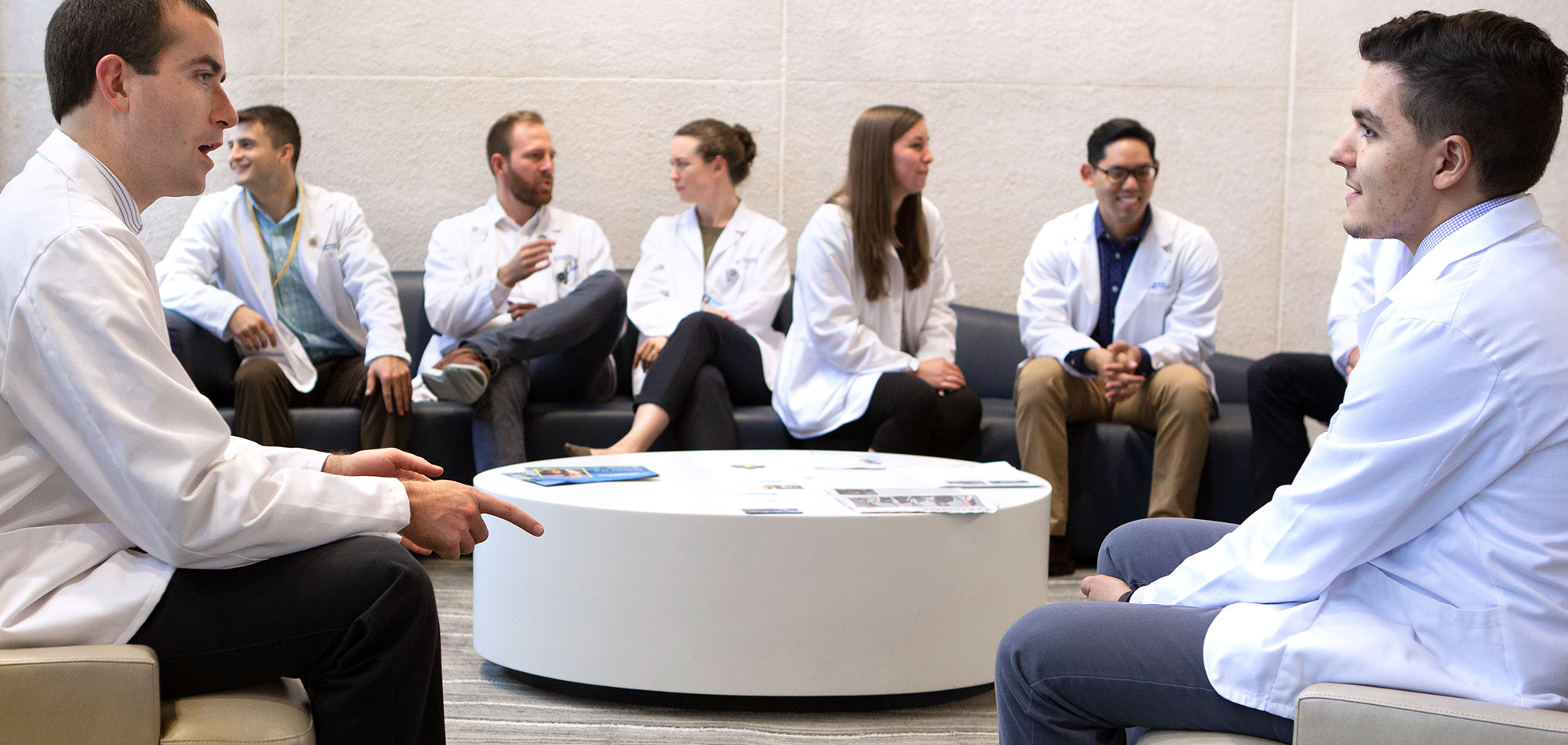 Students in the accelerated (3+) MD programs at Penn State College of Medicine are pictured in 2019 seated in the lobby of the college on modern-looking chairs. An oblong coffee table is in front of the students. Pictured are, from left, Seth Martin, FM-APPS; Frank Striale, FM-APPS; Dennis Madden, NS-APPS; Elizabeth Zimmerman, IM-APPS; Shannon Brumbaugh, FM-APPS; Alexander Lee, EM-APPS; and Abdel Mohamed, FM-APPS.
