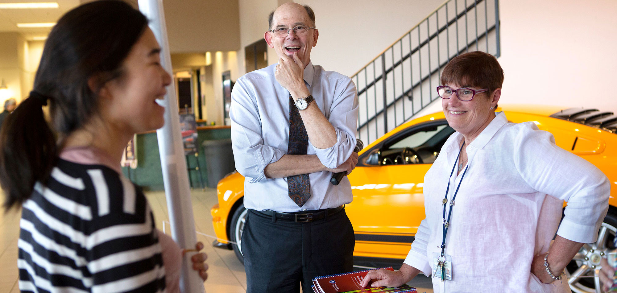 A graduate student is seen laughing with Dr. Charles Lang, Associate Dean for Graduate Education, center, and Kathy Simon, Director of Graduate Education, right, at the 2018 Faculty and Student Research Retreat. The three are pictured standing in front of a car in a museum.