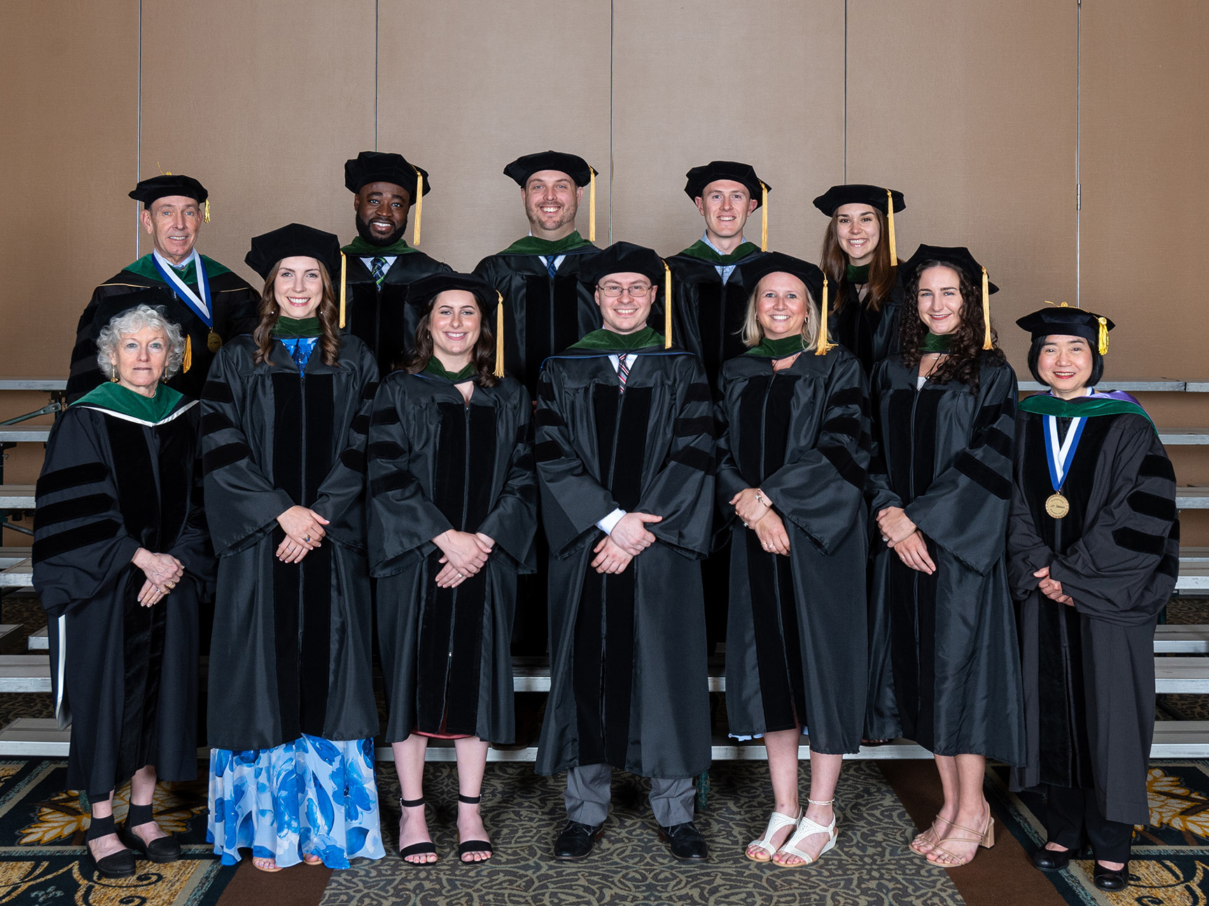 Nine graduating MD students wearing commencement robes and caps pose for a photo, flanked by two members of leadership on the left and one on the right. 