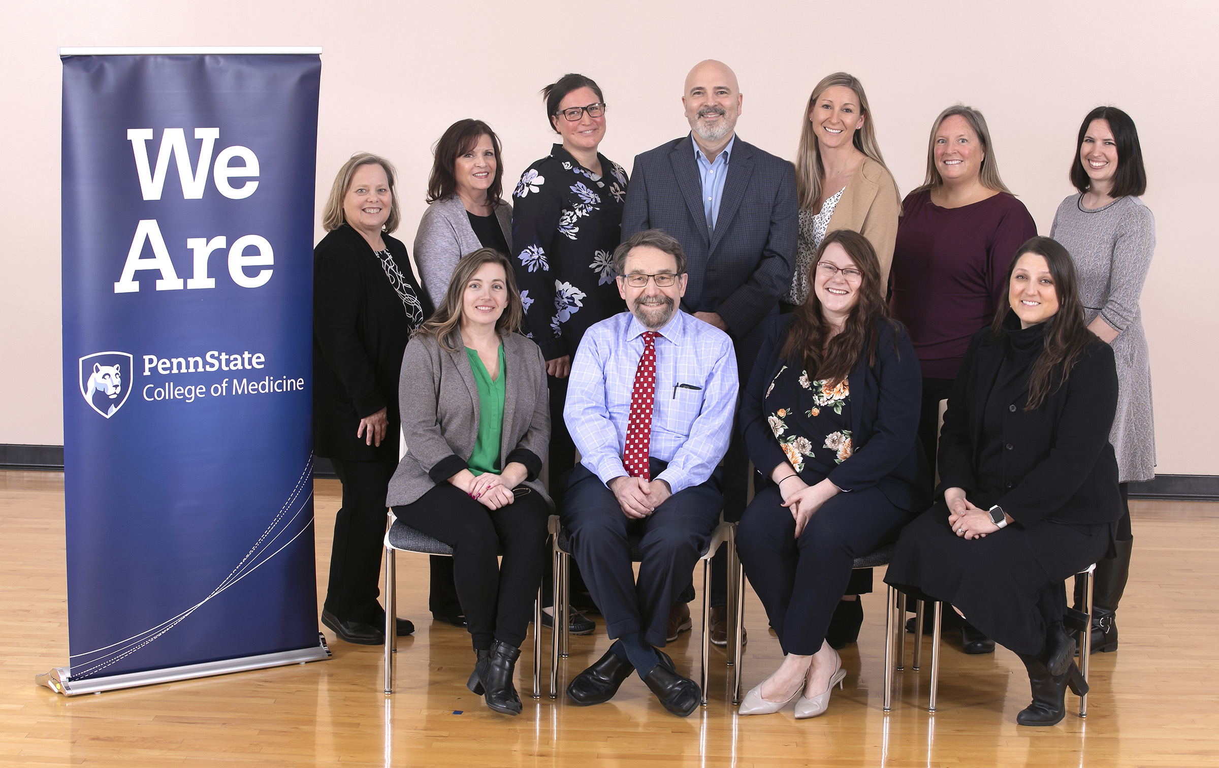 Physician Assistant Program faculty and staff, four seated in front and seven standing behind, are pictured next to a We Are Penn State College of Medicine banner.