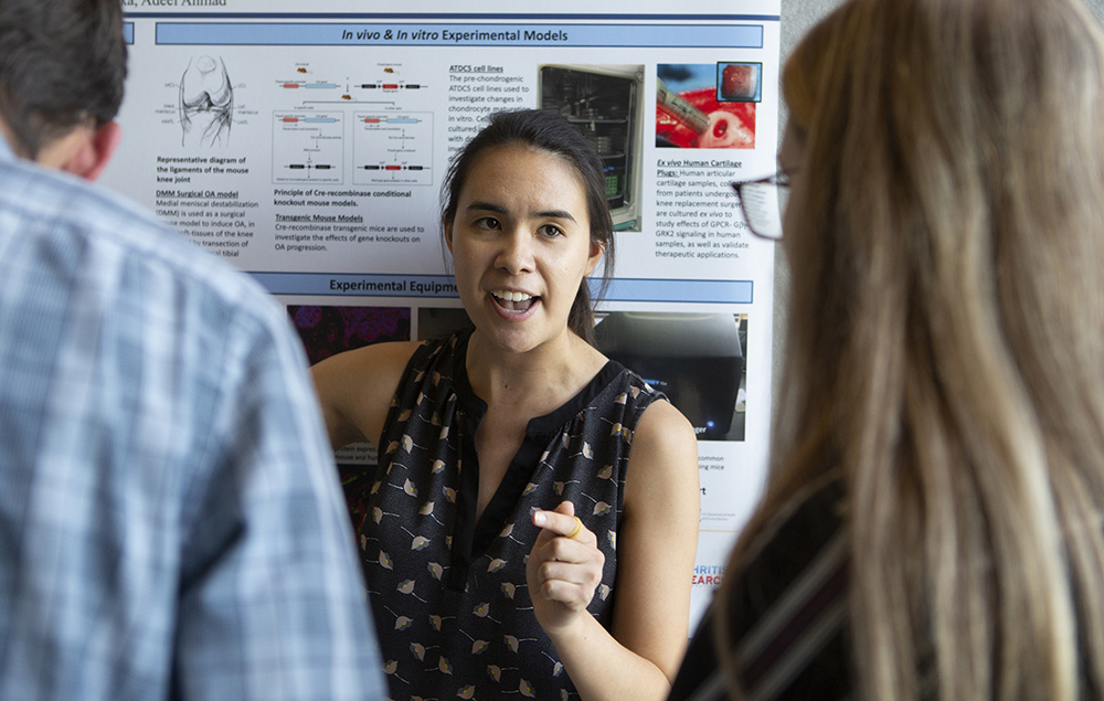 A photo of Natalie Yoshioka presenting her poster project to others.