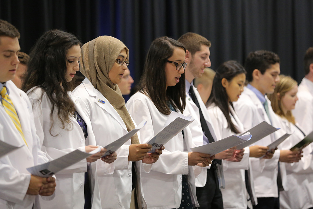A diverse group of students in white coats standing together and reciting an oath during the 2017 College of Medicine White Coat Ceremony.