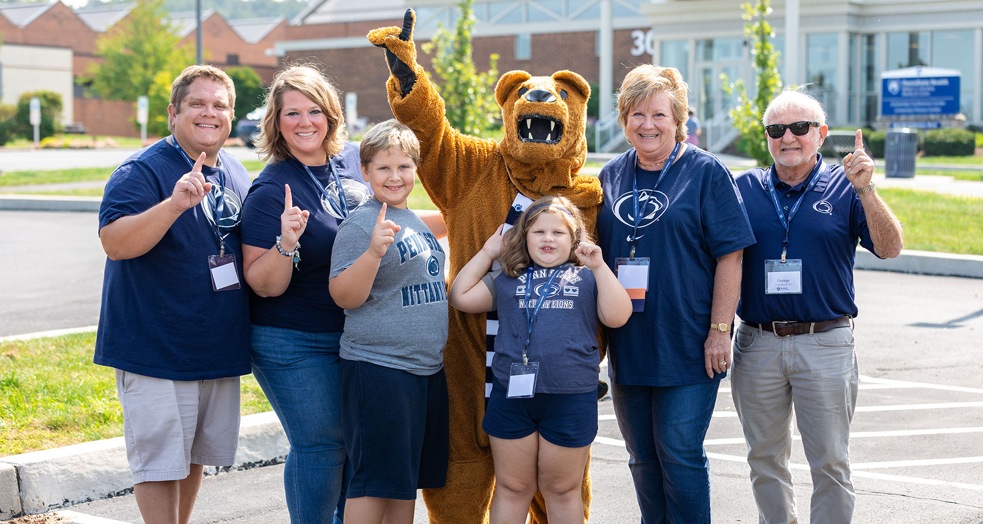 A group of people wearing Penn State clothing pose and give the No. 1 hand sign with the Nittany Lion mascot.